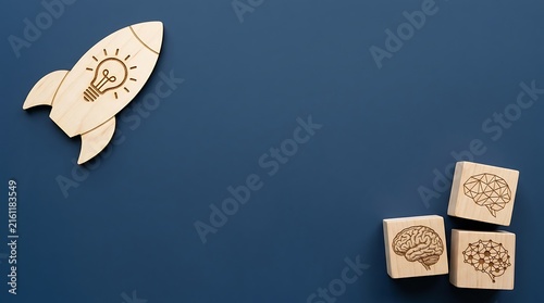 Wooden rocket ship with lightbulb design next to three wooden blocks featuring brain illustrations for creative business strategy development concepts on deep blue background surfaces.