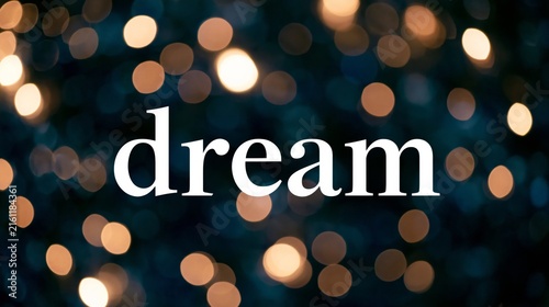 Dream word in elegant white typography over a dark blue background with warm glowing bokeh lights