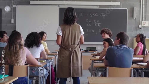 High school students concentrated during exam with teacher watching them, walking around. Footage with copy space.
