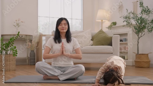 Woman and child meditation yoga exercise on yoga mat in bright living room, calm family wellness living scene with sitting, natural plants, sofa, soft home lighting, peaceful mindful practice