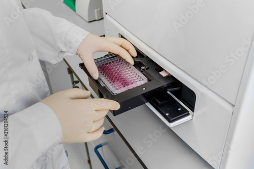 Фотография Scientist in gloves inserting a microplate with samples into a laboratory analyzer
