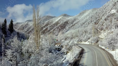 Aerial view of a car driving on a winding mountain road surrounded by snow-covered winter forest