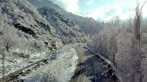 Aerial view of cars driving on scenic winding mountain road surrounded by snow-covered forest and river in winter