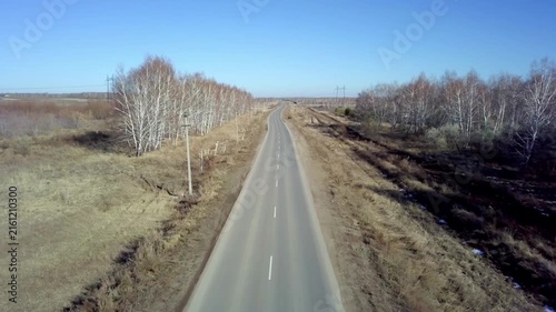 Aerial view of a red car driving on country asphalt road through birch forest in autumn