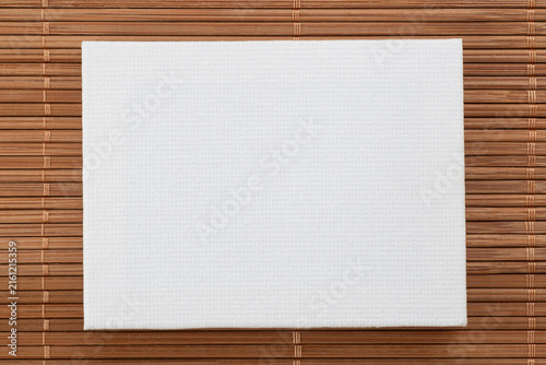 blank white artist canvas laying on brown bamboo mat