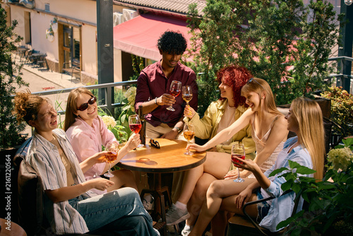 Large group of friends relaxing with wine on outdoor terrace. Concept of shared experiences, group connection, weekend gatherings, hospitality and wine lifestyle marketing.