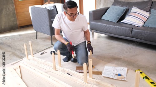Focused man using tool for wood furniture assembly at home, building wooden frame on living room floor