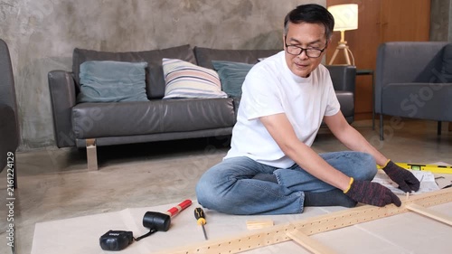 Furniture assembly man using tool on living room floor, focused worker building wooden cabinet beside sofa
