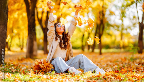 Konstfotografi Young woman sits in clearing in park strewn with autumn leaves at sunset