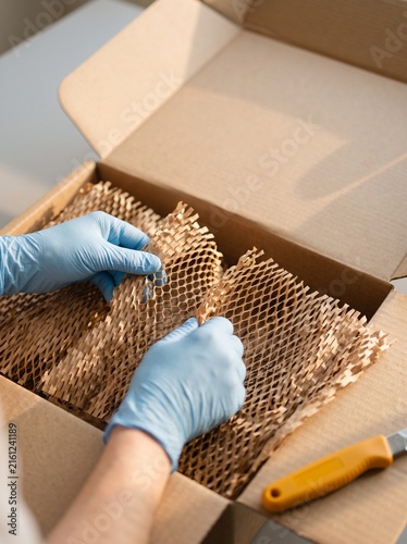 Hands in blue protective gloves unpacking sustainable honeycomb paper wrapping inside a cardboard shipping box