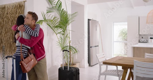 Couple entering home pulling suitcase, hugging and dancing beside potted palm, deciding next step