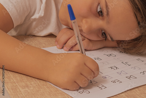 Bild auf Leinwand Close up view of a sad reluctant kid practicing handwriting on a dotted paper sh