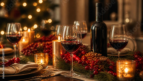 Festive christmas table setting with red wine glasses, a bottle of wine, candles, and holiday decorations, creating a warm and cozy atmosphere for a holiday dinner celebration