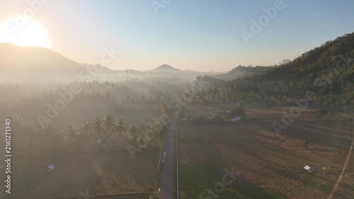 Beautiful golden sunrise over misty rice fields and coconut palm trees with mountain background in Dusun Tempos Desa Banyu Urip Gerung Lombok NTB Indonesia