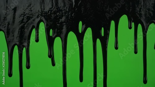 Black liquid dripping down a green screen during a slow motion close up