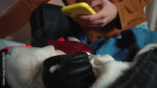Anonymous young woman preparing her suitcase while getting distracted by her smartphone, pausing her packing to check her phone during a travel preparation moment.