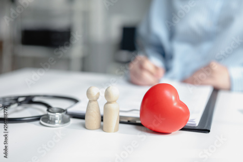 Obraz na plátně Wooden dolls with red rubber heart and medical stethoscope on insurance policy form table