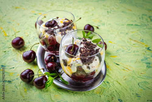 Parfait dessert with whipped cream,  mascarpone fresh cream cheese, dark chocolate and sour and sweet cherries served as close-up in a glass