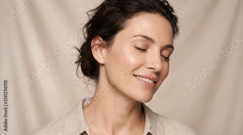 Smiling woman with curly hair in updo looking down with peaceful expression against neutral fabric