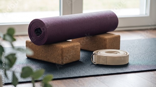 Purple rolled yoga mat resting on cork blocks and strap on a black mat indoors with exercise