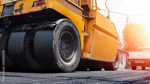 Yellow road roller compactor working on freshly paved asphalt, showing heavy construction machinery used for roadwork, pavement repair, street maintenance and infrastructure development.