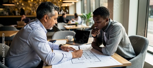 Senior mentor and young apprentice reviewing blueprints in cafe