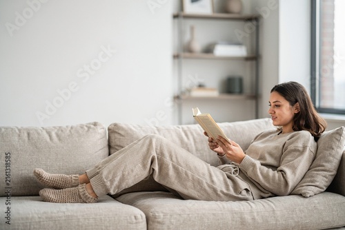 Person reading book while relaxing on sofa in bright home