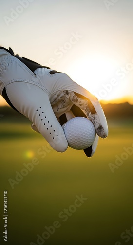 Golfer Hand Holding Golf Ball on Beautiful Green Course During Sunset