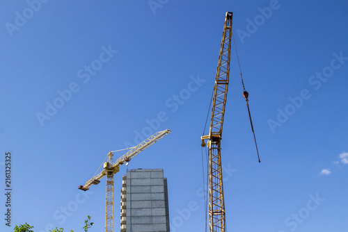 Two construction cranes and the facade of a building under construction. Blue sky. Part of the frame