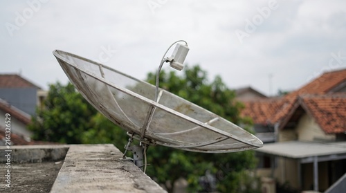 Satellite dish on residential rooftop, metal parabolic antenna for television signal, telecommunications equipment in urban neighborhood