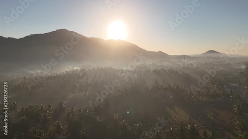 Beautiful golden sunrise over misty rice fields and coconut palm trees with mountain background in Dusun Tempos Desa Banyu Urip Gerung Lombok NTB Indonesia