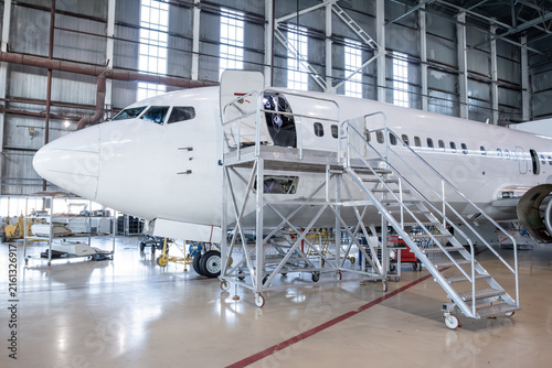 White passenger aircraft in the aviation hangar. Jet plane under maintenance. Checking mechanical systems for flight operations