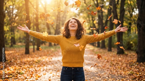 Smiling young woman in a forest clearing, arms outstretched in mustard sweater and jeans, looking up as autumn leaves fall around her in warm sunlight. No text