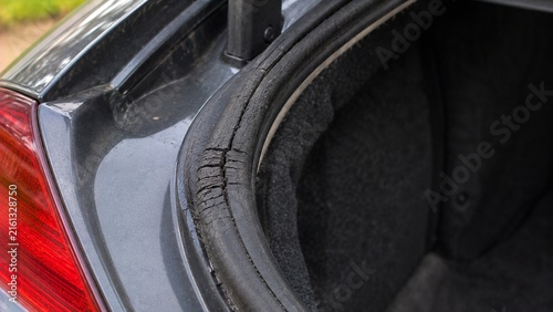Close-up of vehicle trunk opening showing aging rubber weather seal with visible cracking and compressed damaged section that could allow water intrusion