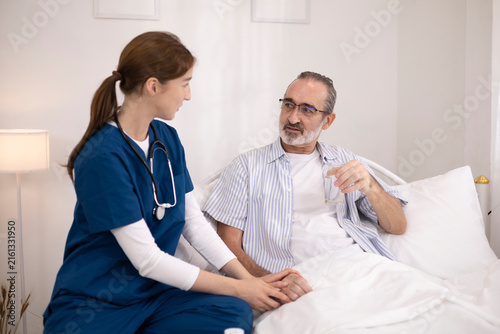 The elderly man was being cared for at home by a private nurse for his illness. The nurse brought him medication to take before bedtime and checked on his condition to monitor his health.