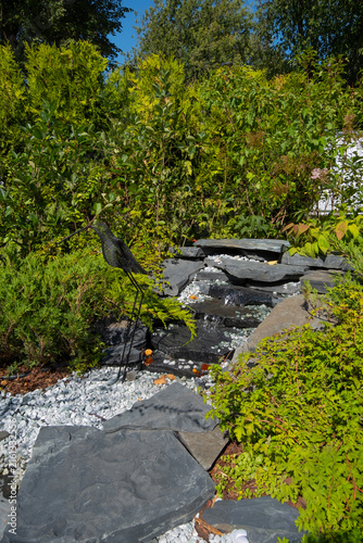 Konstfotografi Bird sculpture near water feature in a garden surrounded by greenery on a sunny