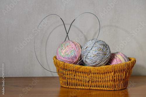 Basket filled with colorful yarn balls and circular knitting needles on a wooden table