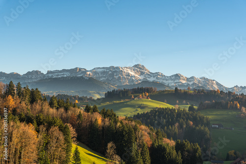 Autumn landscape with rolling green hills and the Alpstein mountains and Saentis peak on the horizon near Herisau, Canton of Appenzell Ausserrhoden, Switzerland