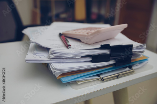 Stack of financial documents with a calculator and pen on a desk, representing tax calculation, accounting, budgeting, financial planning, and paperwork management.
