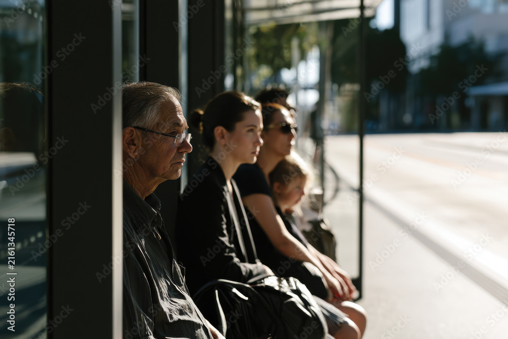 Fototapeta premium A similar scene to another bus stop captures an elderly man and diverse individuals waiting, showcasing the essence of shared public transport experiences in urban life.