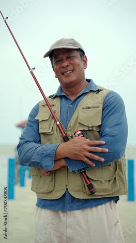 Happy senior man sitting by the sea and fishing with a rod after retirement. Active aging, healthy longevity, outdoor leisure, fulfilling retirement. Life insurance and financial security concept.
