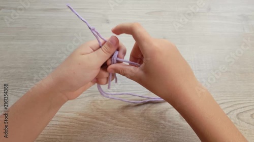 Child Hands Tying a Knot with Purple Rope on Wooden Table