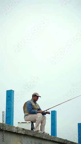Happy senior man sitting by the sea and fishing with a rod after retirement. Active aging, healthy longevity, outdoor leisure, fulfilling retirement. Life insurance and financial security concept.
