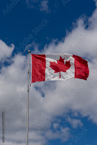 Photography A National Flag of Canada waving against a blue sky with white clouds