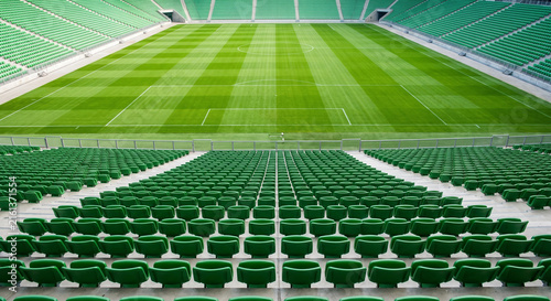Wide angle symmetrical view of empty football stadium with green seats and manicured pitch