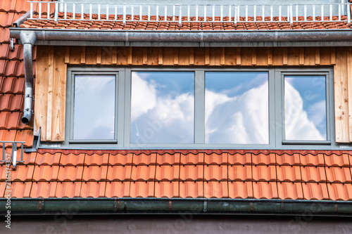 Weiße Wolkengebilde vor blauem Himmel spiegeln sich in Fensterfront an Dachgeschosswohnung mit Ziegeldach mit Regenrinne, Regenfallrohr und Schneefanggitter in Neckartenzlingen