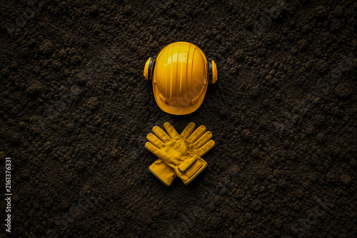 Yellow hard hat and protective gloves on dark industrial soil, symbolizing workplace safety and occupational protection.
