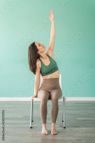Fotografía Woman stretches upward, seated on a chair