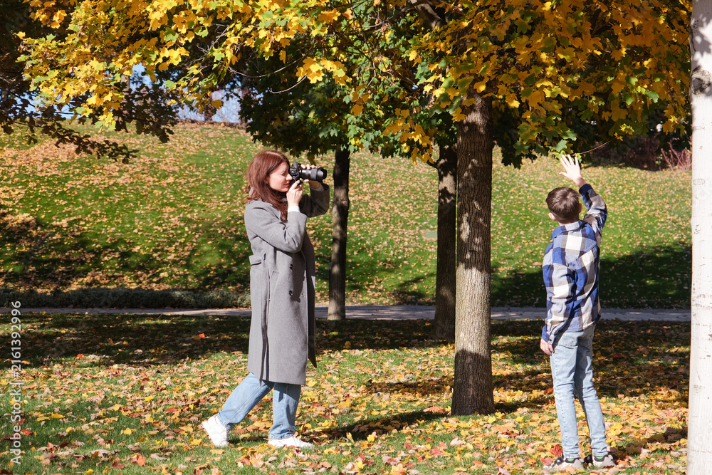 Fototapeta premium adult woman taking pictures of son in autumn leaves in the park or forest