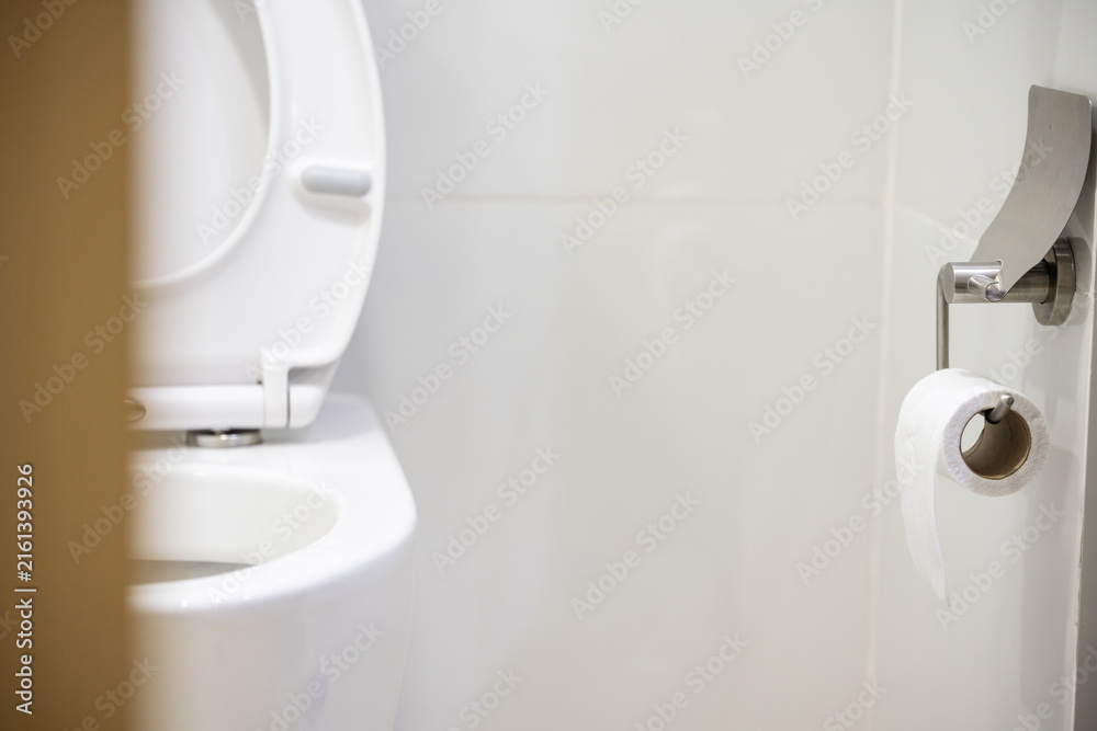 Fototapeta premium White toilet bowl and tissue paper roll in the bathroom at home.Ceramic wc bowl and roll of toilet in bathroom with modern interior.Modern toilet concept.